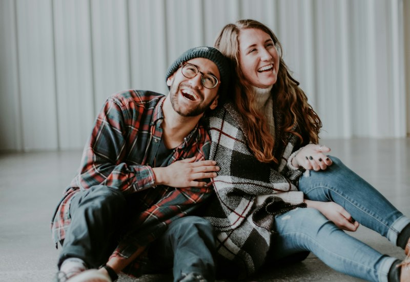 A man and a woman laughing together while sitting on the floor in casual clothes