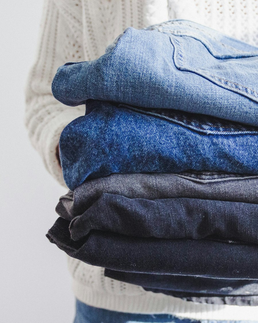 A person in a cream knit sweater holding a stack of folded denim jeans